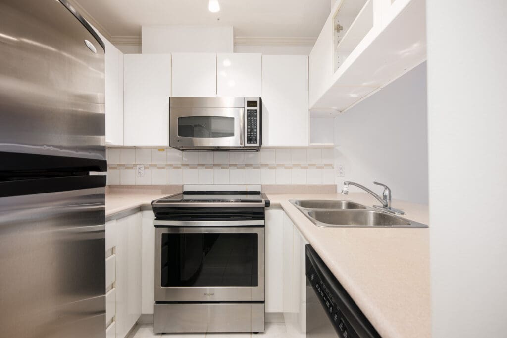 Modern kitchen with stainless steel appliances, white cabinets, a double sink, and beige countertops arranged in a compact U-shaped layout.