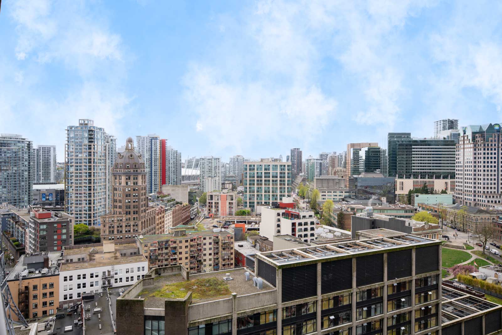 A cityscape view featuring modern and historic high-rise buildings under a partly cloudy blue sky.