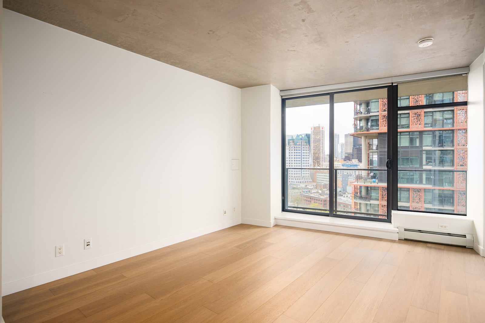Unfurnished modern apartment room with light wood floor, white walls, large window, and city view.