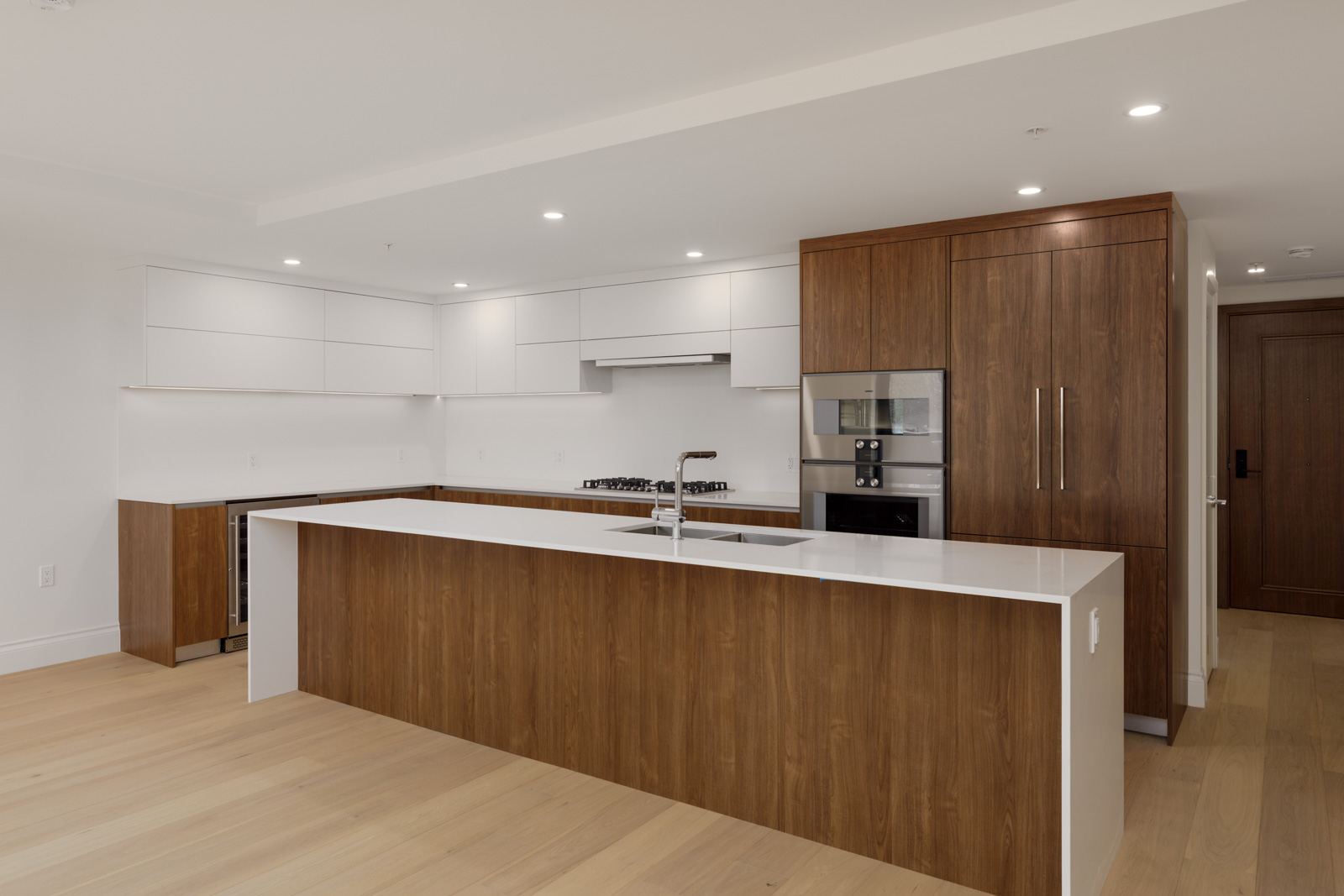 Modern kitchen with white countertops, wood cabinets, built-in appliances, gas cooktop, and light wood flooring.