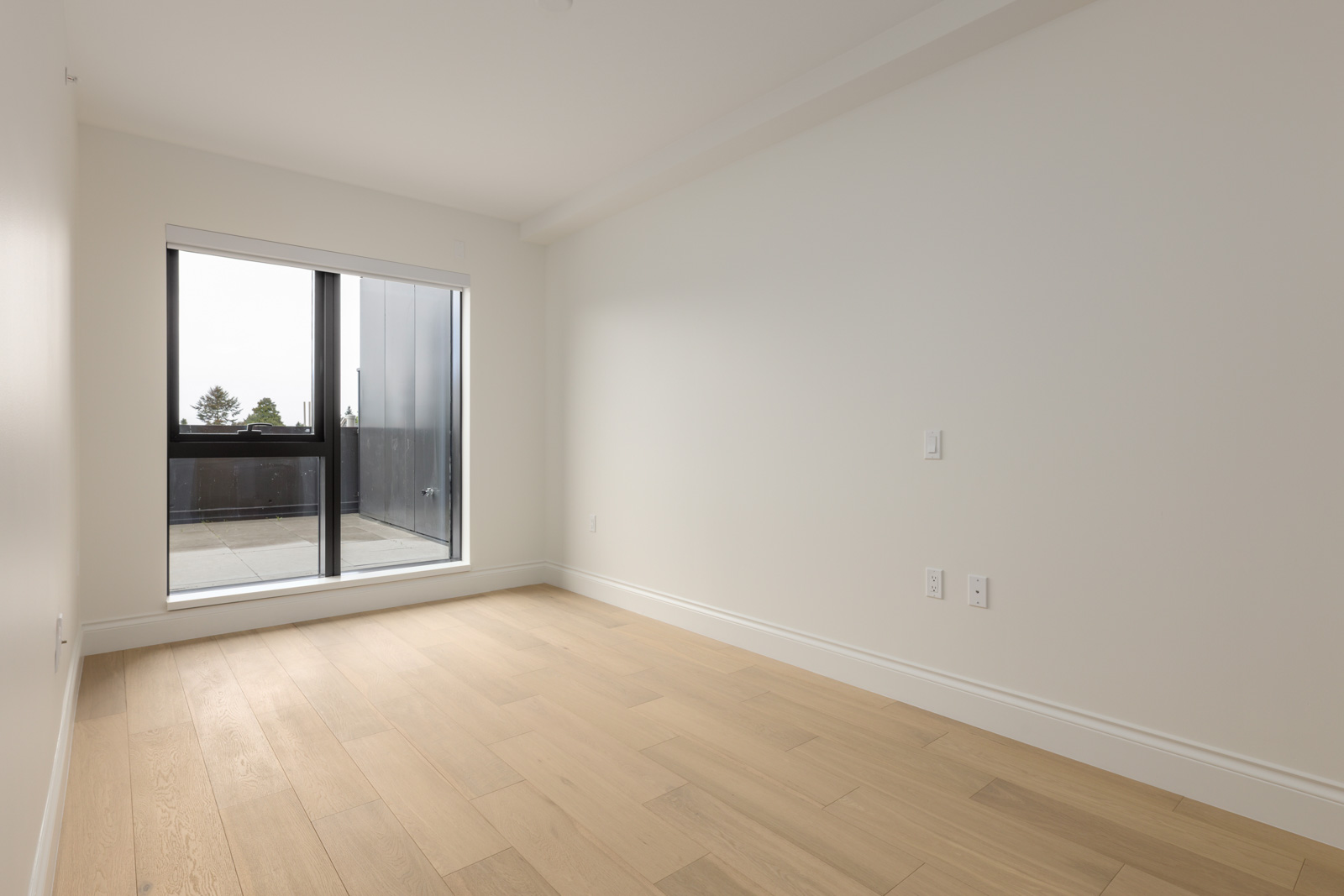 Unfurnished room with light wood flooring, white walls, and a large window leading to a balcony.