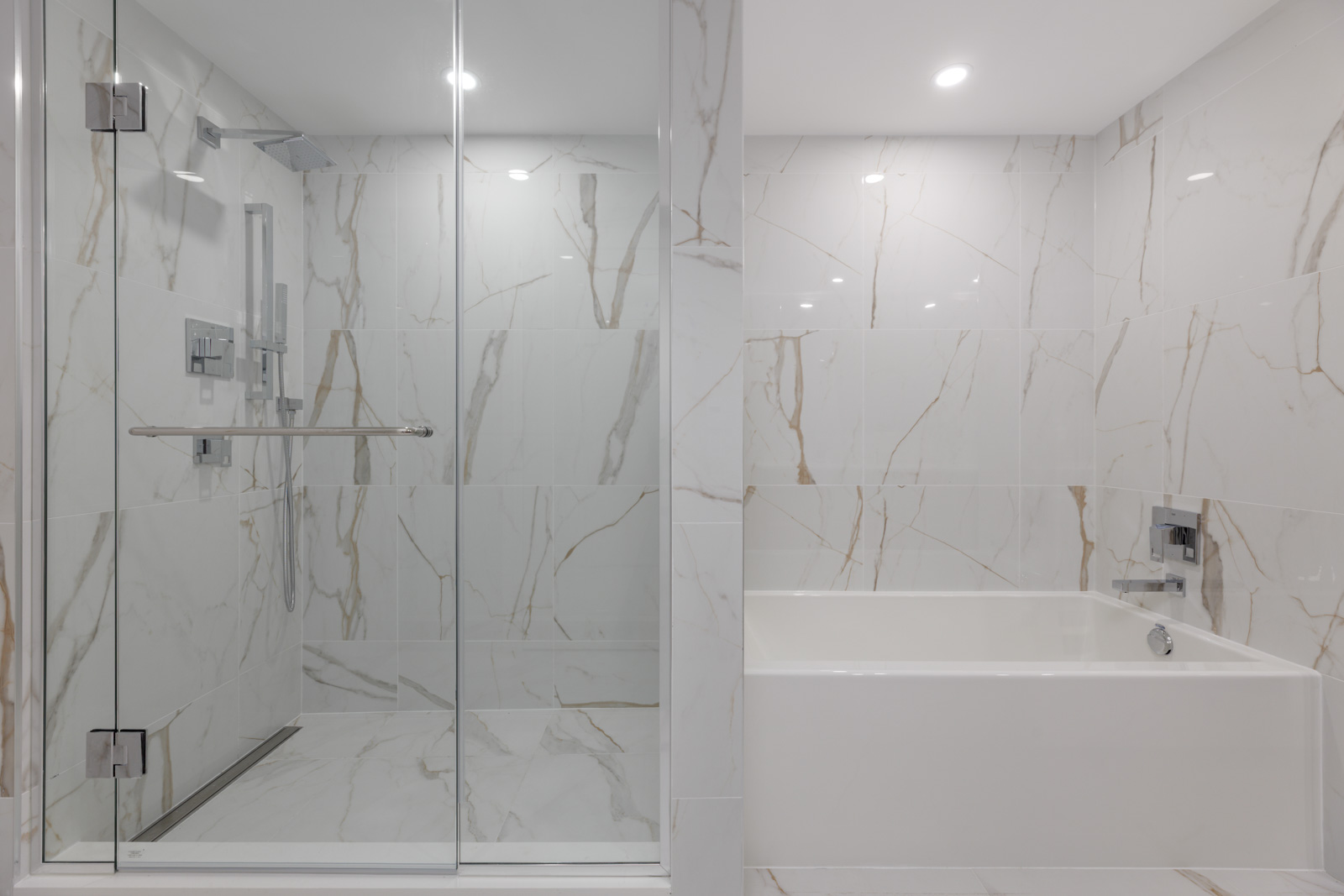Modern bathroom with a glass-enclosed shower and a separate white bathtub, both surrounded by white marble tiles with beige veining.