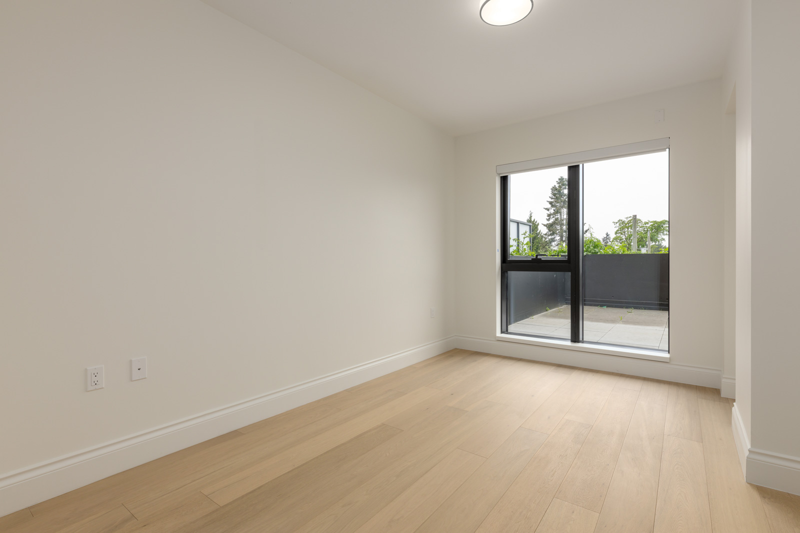 Empty room with light wood flooring, white walls, and large window door leading to an outdoor patio area.