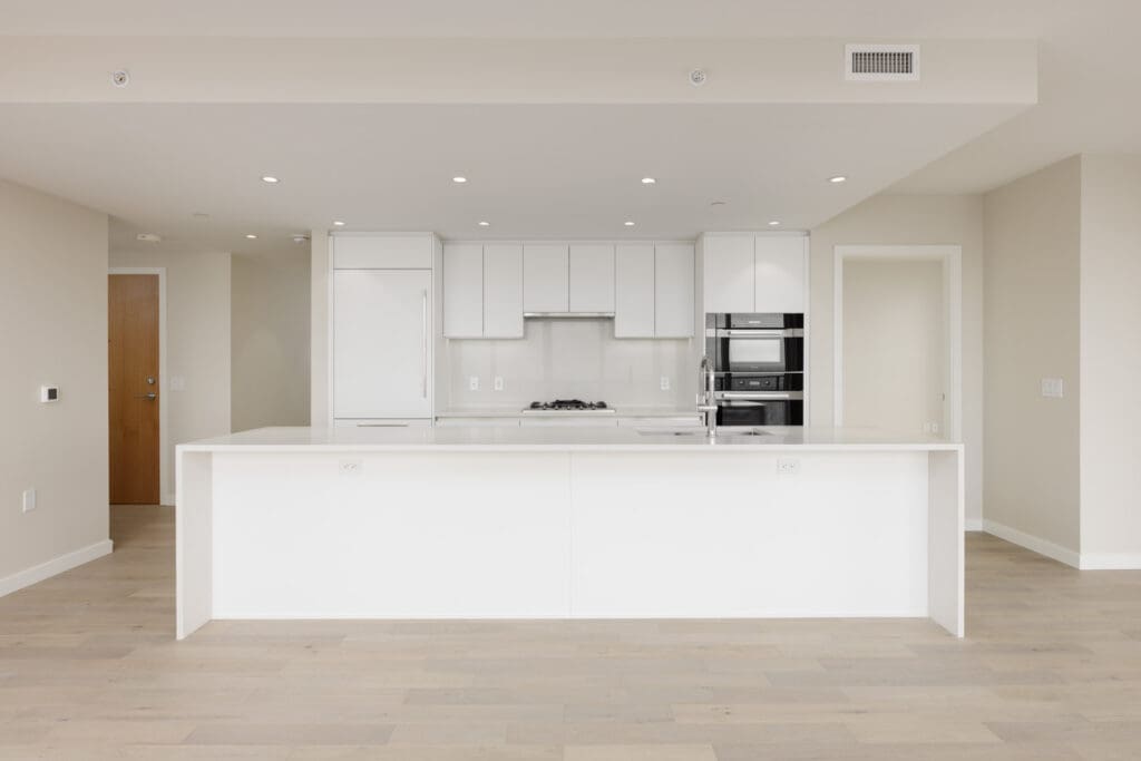 Modern kitchen with white cabinetry, built-in appliances, a central island, light wood flooring, and neutral-colored walls.