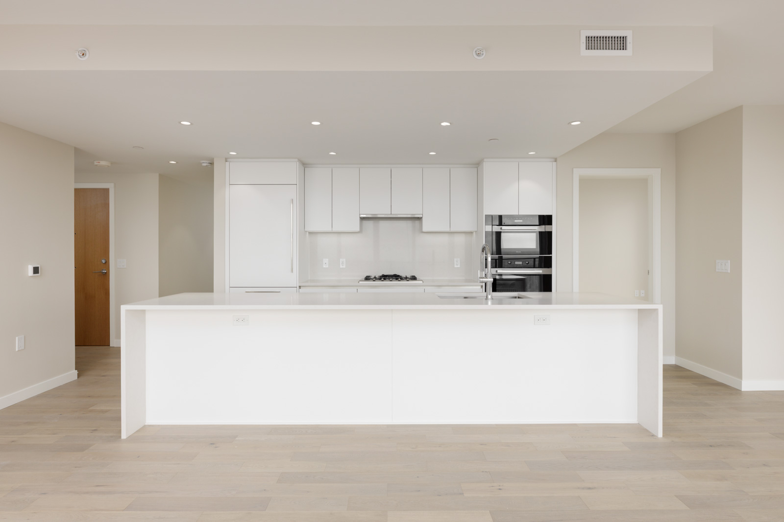 Modern kitchen with white cabinetry, built-in appliances, a central island, light wood flooring, and neutral-colored walls.