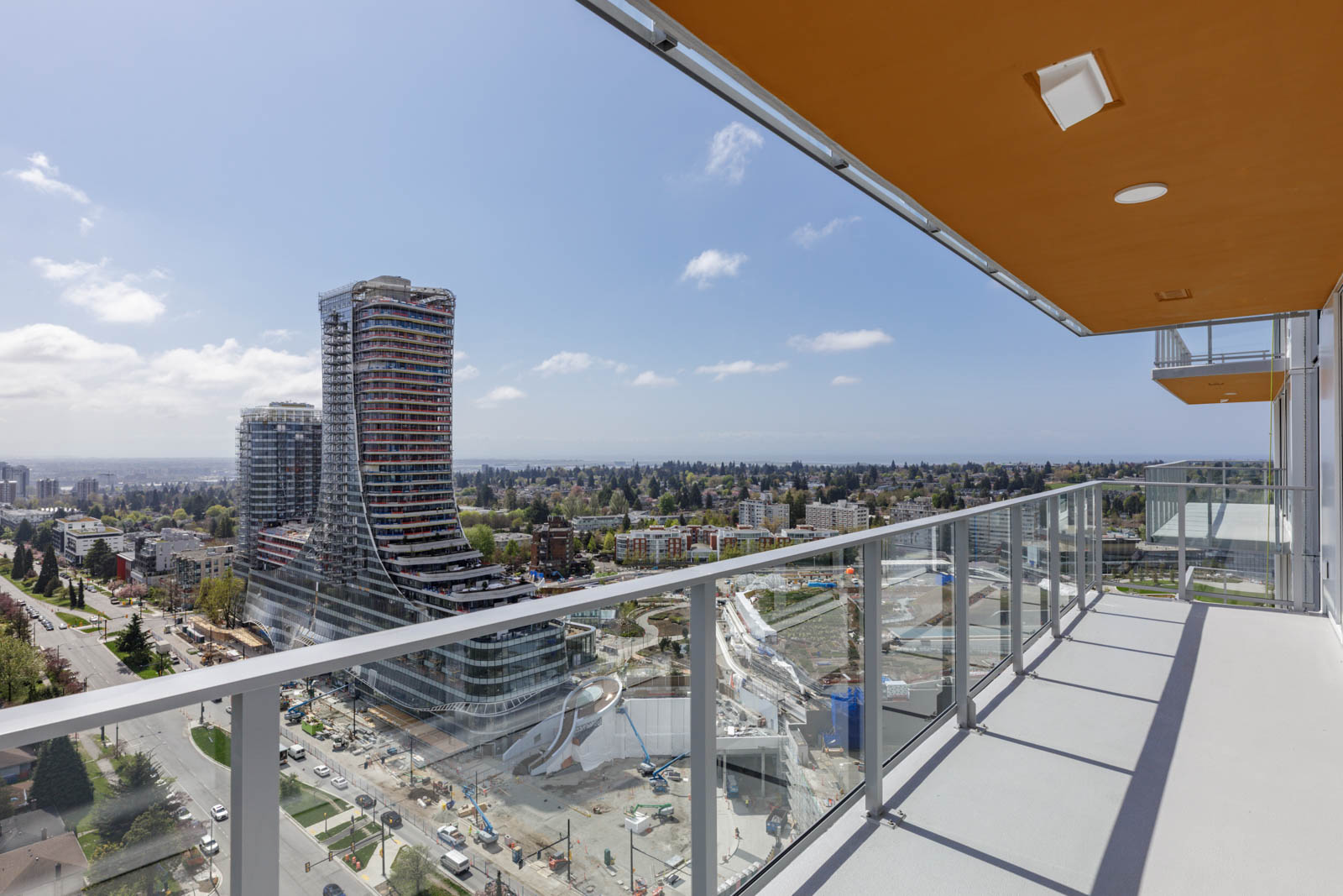 View from a high-rise balcony overlooking a modern cityscape with tall curved buildings, a park, and clear skies.