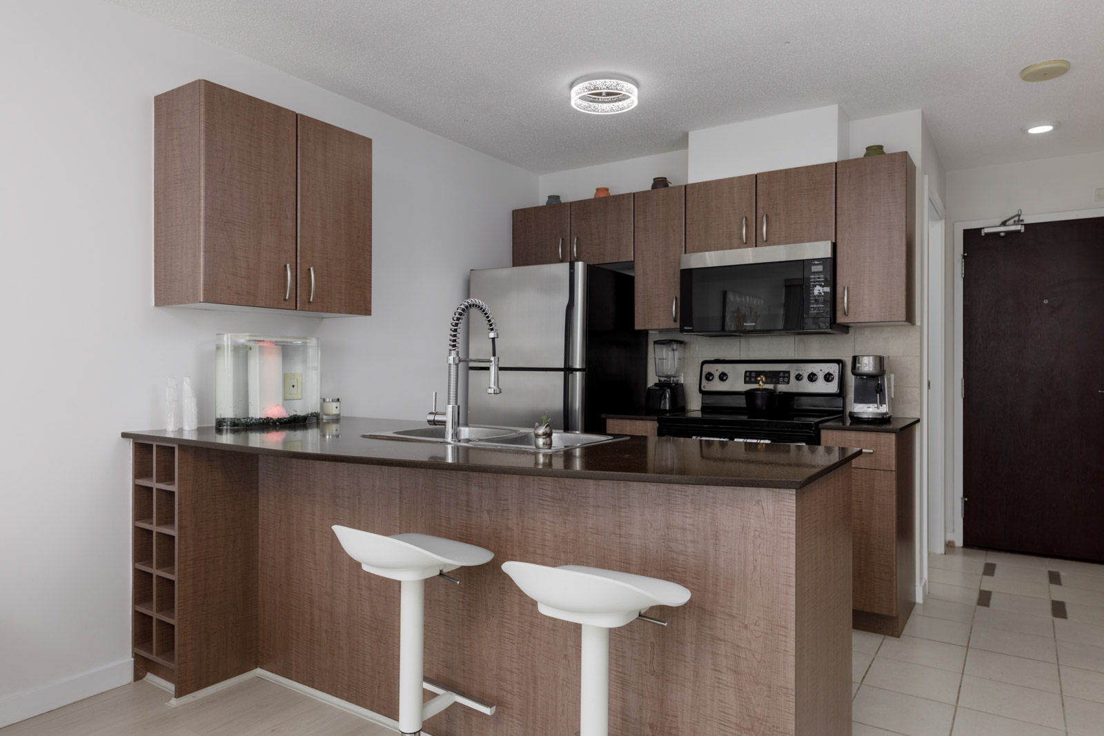 Modern kitchen with brown cabinets, stainless steel appliances, an island with a sink, and two white bar stools.