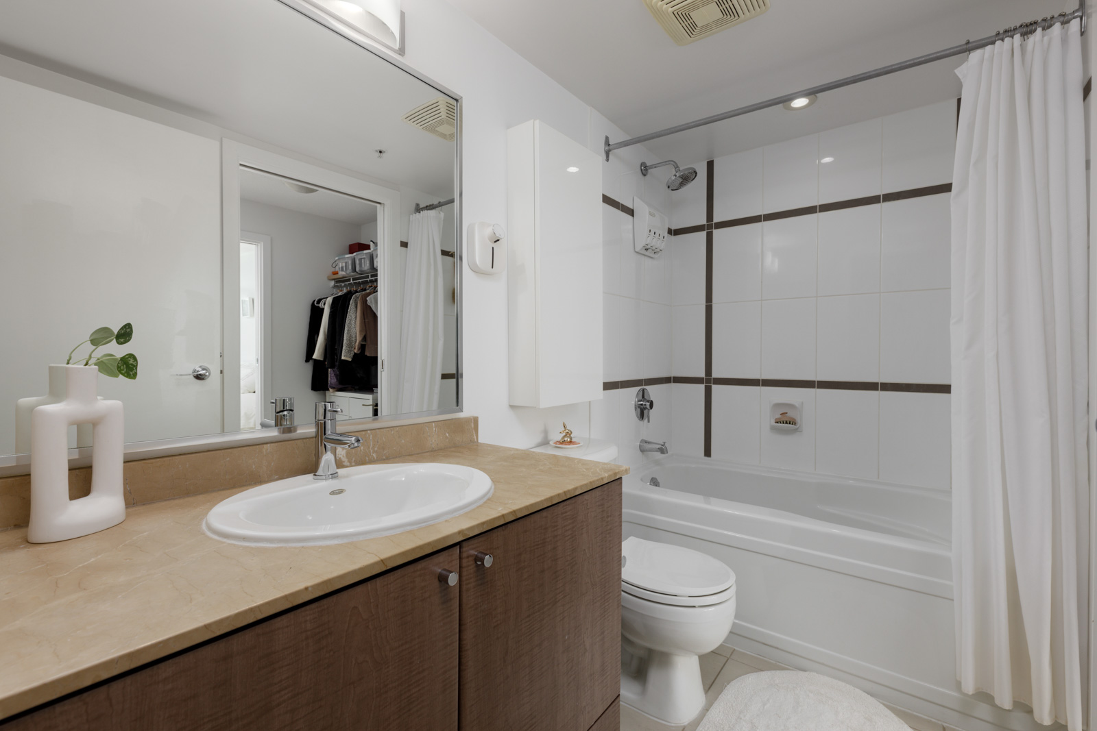 Modern bathroom with a sink, countertop, toilet, bathtub with shower curtain, and a closet visible through an open door.