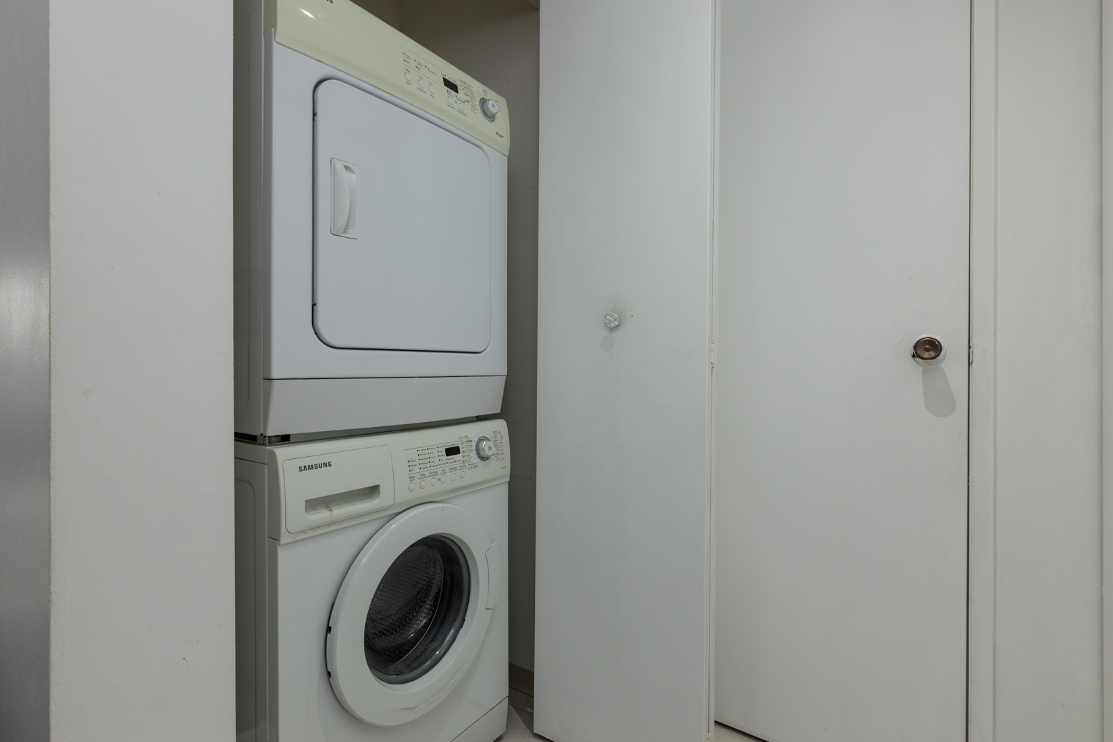 Stacked washer and dryer unit in a small laundry area with white walls and closed doors.