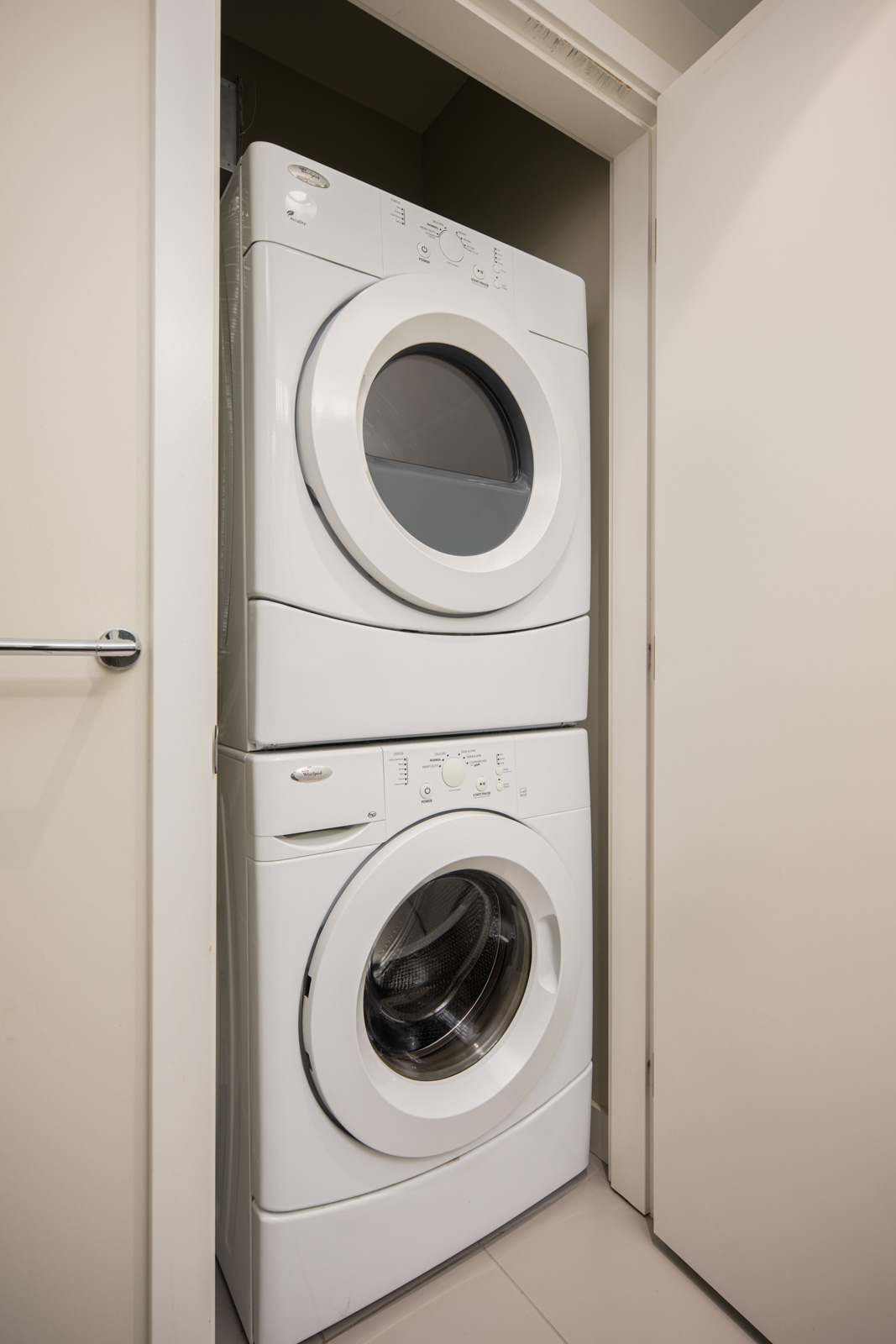 A white stacked washer and dryer set is placed in a small laundry closet with the door partially open.