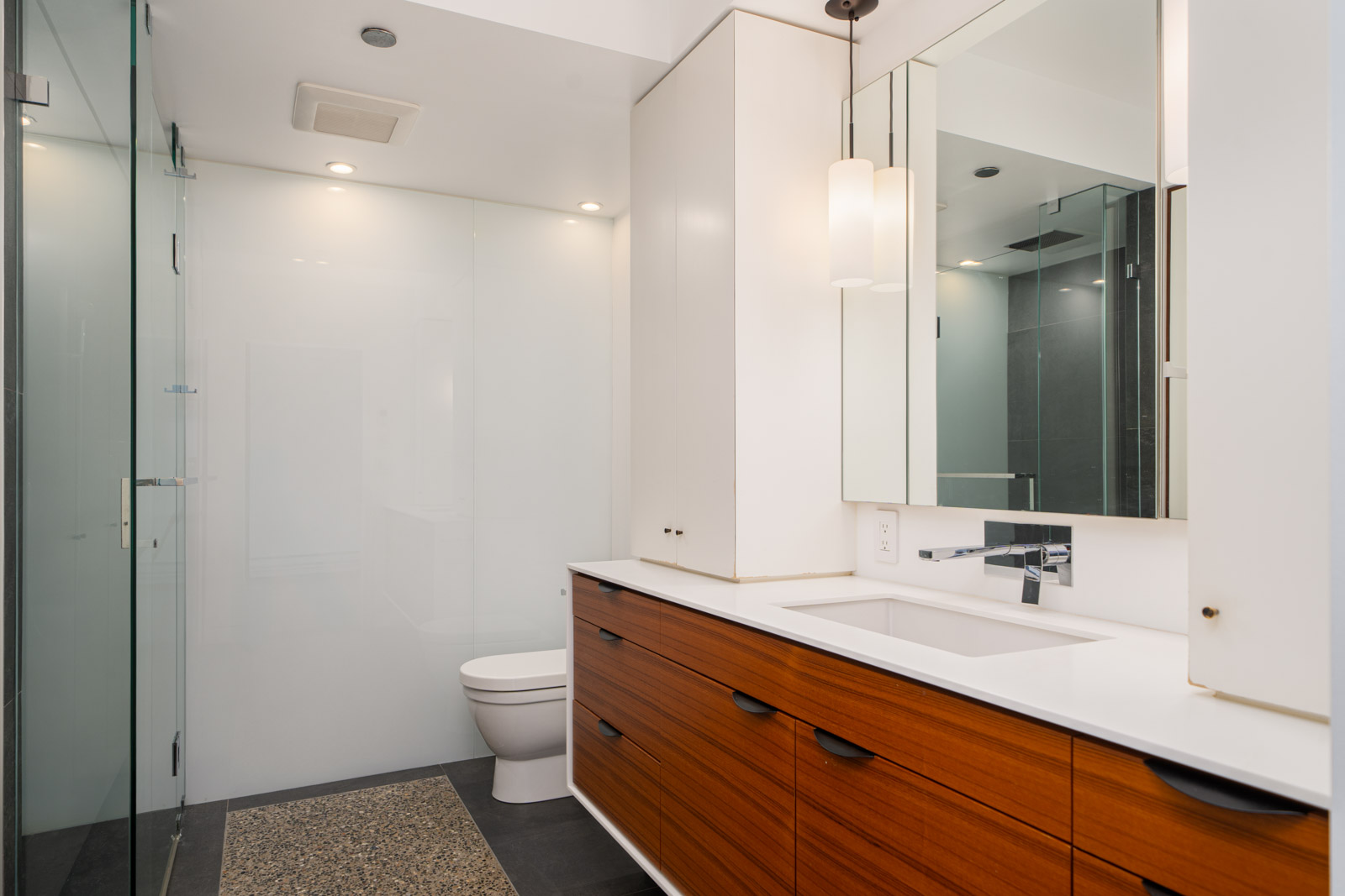 Modern bathroom with a glass-enclosed shower, white walls, wooden vanity with drawers, a white countertop, and a large mirror above the sink.