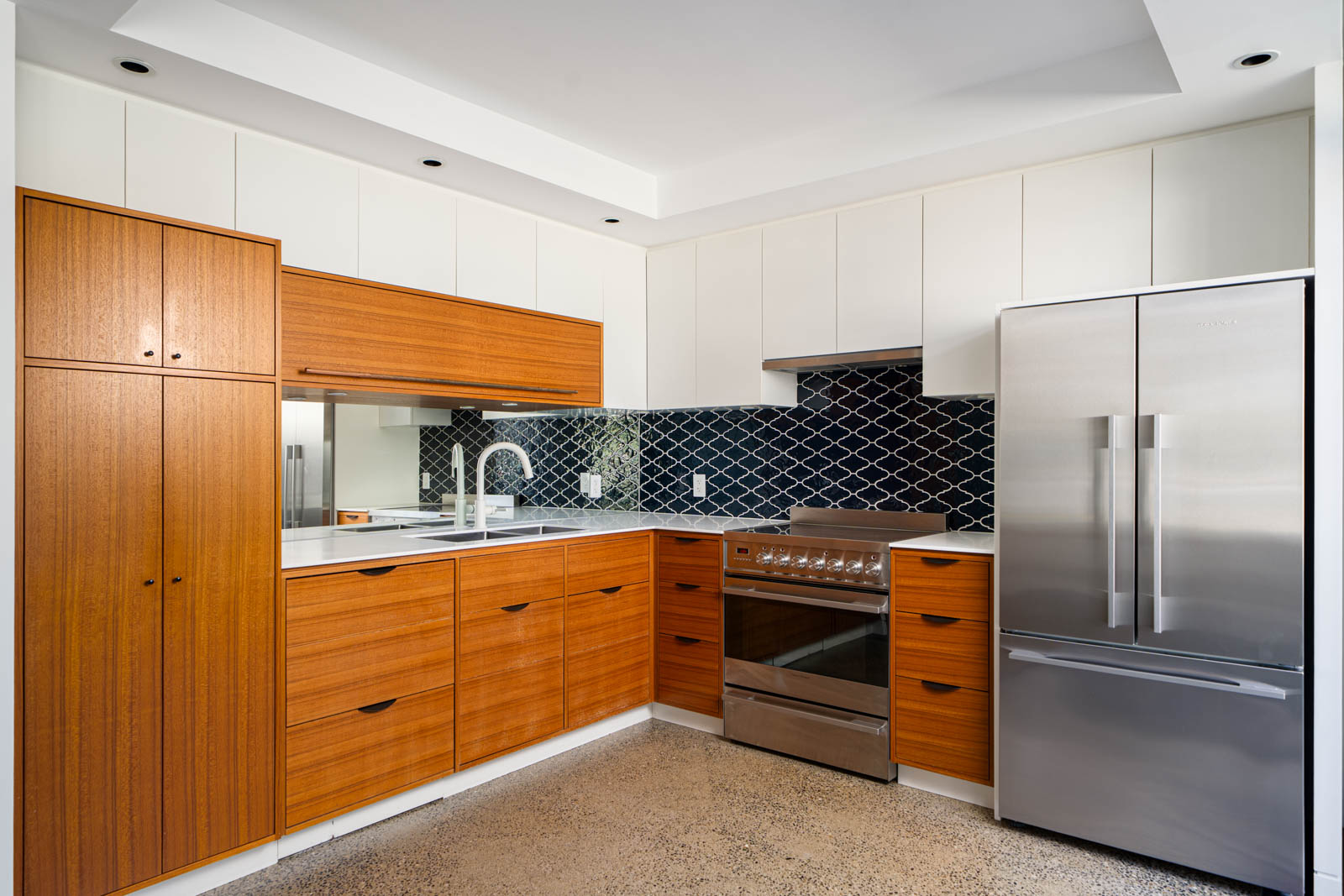 Modern kitchen with wood cabinets, stainless steel appliances, white countertops, and a black geometric tile backsplash.