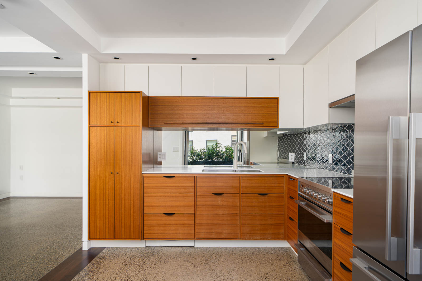 Modern kitchen with wood cabinets, white upper cabinets, stainless steel appliances, a patterned tile backsplash, and a polished concrete floor.