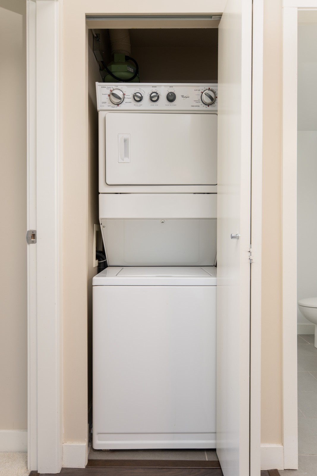 Stacked washer and dryer unit inside a small closet with the door partially open.