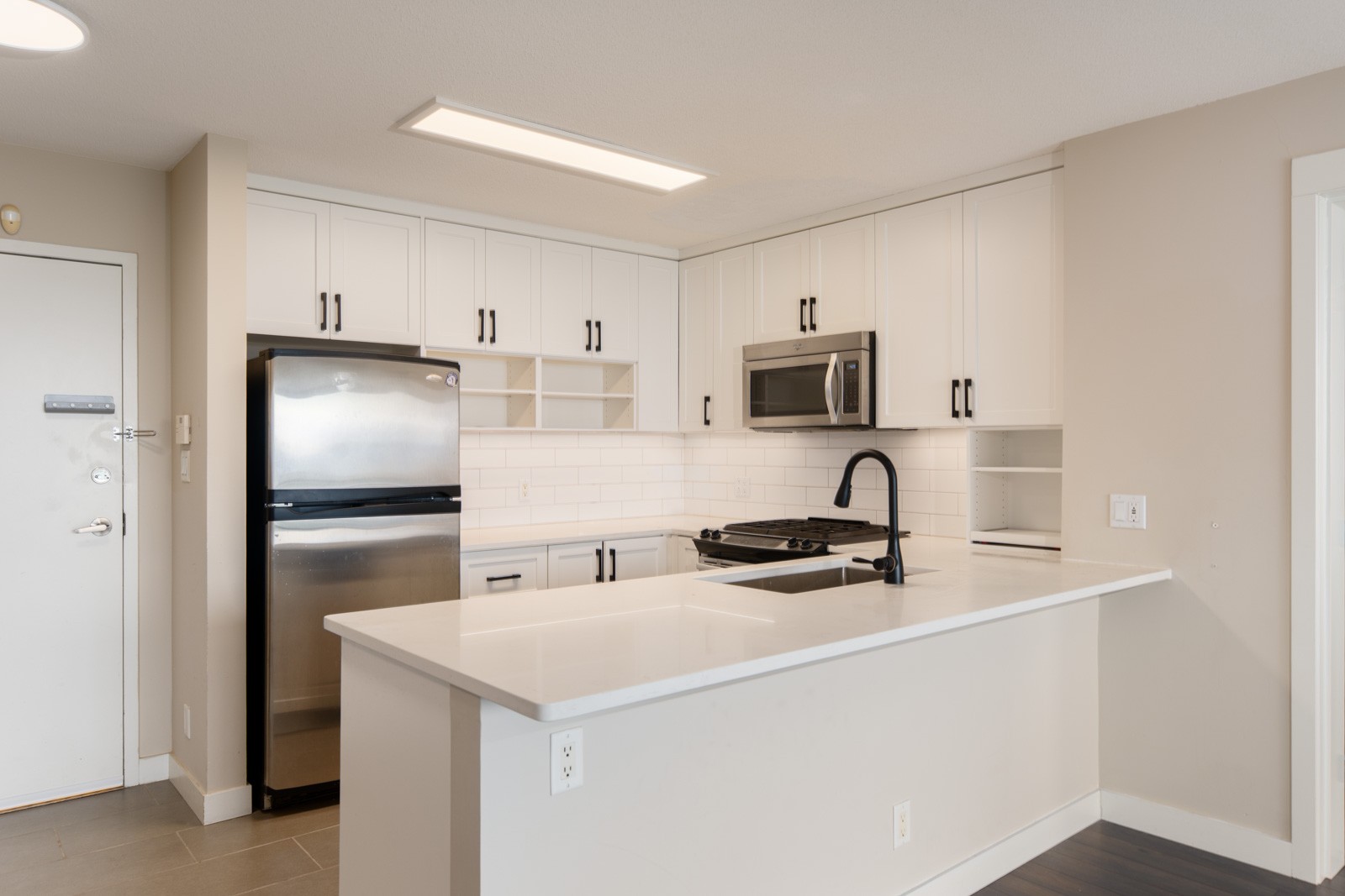 Modern kitchen with white cabinets, stainless steel appliances, a black faucet, and a white countertop with an island.