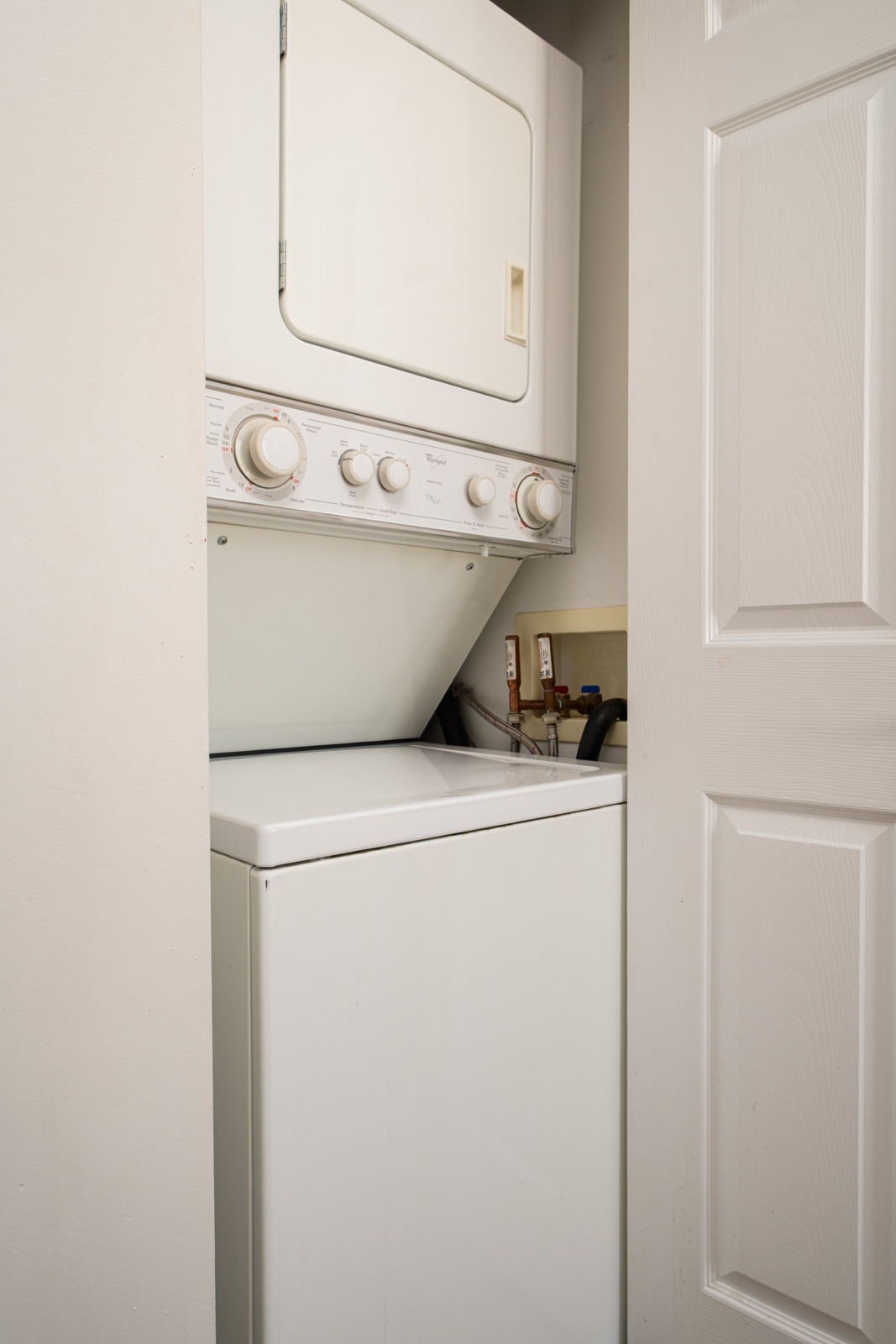A stacked washer and dryer unit is installed in a small laundry closet with white walls and an open door.