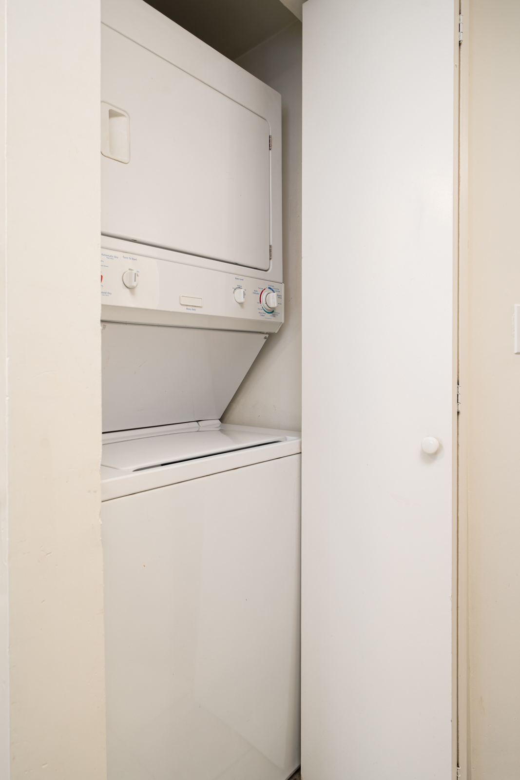 A white stacked washer and dryer unit is installed in a small closet with a partially open white door.