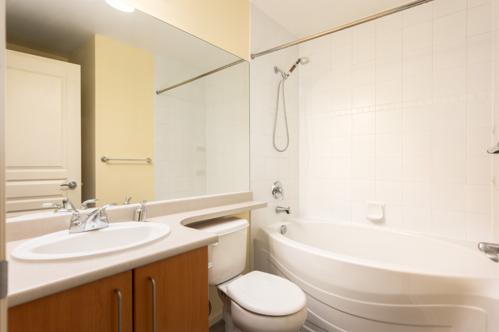 Modern bathroom with a white sink, countertop, toilet, and a bathtub with a showerhead, set against cream and white tiled walls.
