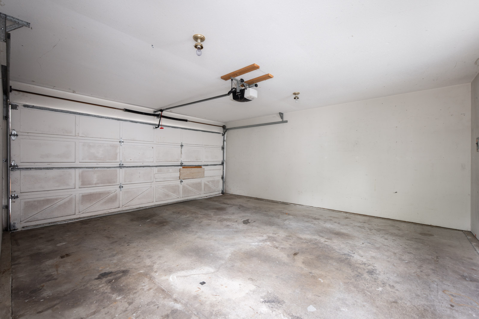 Empty two-car garage with a concrete floor, white walls, and a closed sectional garage door with an automatic opener mounted on the ceiling.