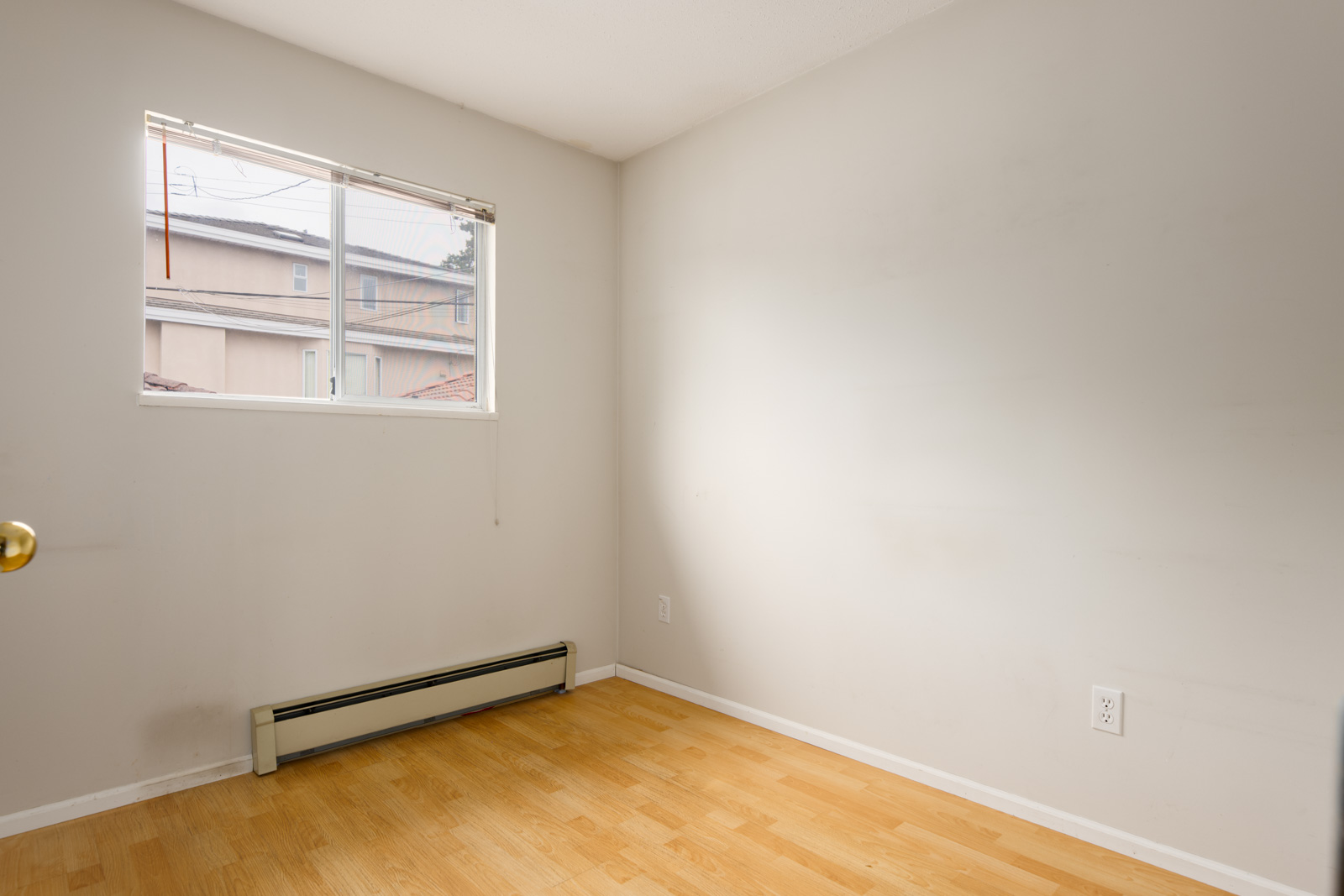 Small empty room with light-colored walls, a single window, baseboard heater, and light wood flooring.