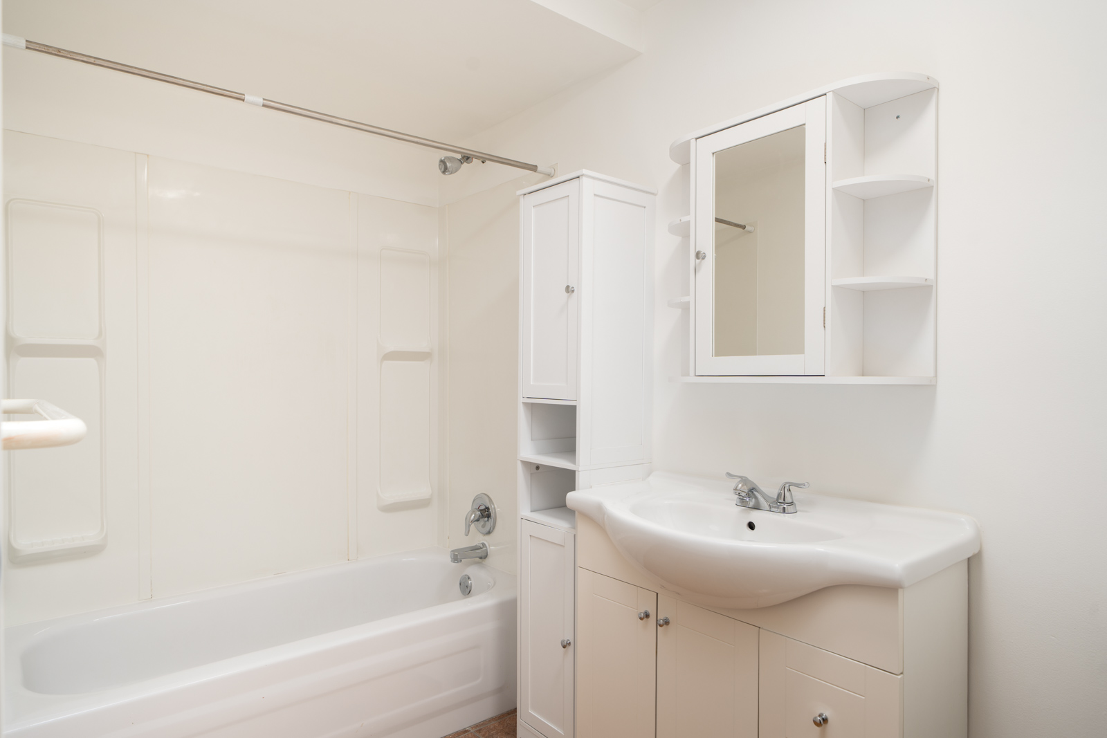 A clean, white bathroom with a bathtub-shower combination, a sink with cabinets, a mirrored medicine cabinet, and a tall storage unit.