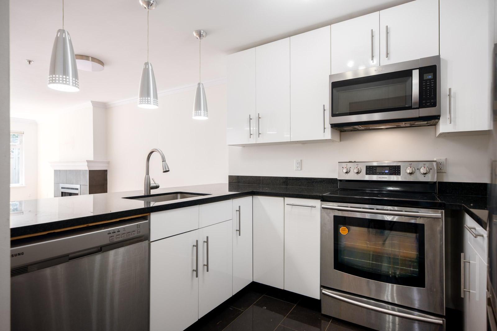 Modern kitchen with white cabinets, stainless steel appliances, black countertops, three pendant lights, and an L-shaped layout.