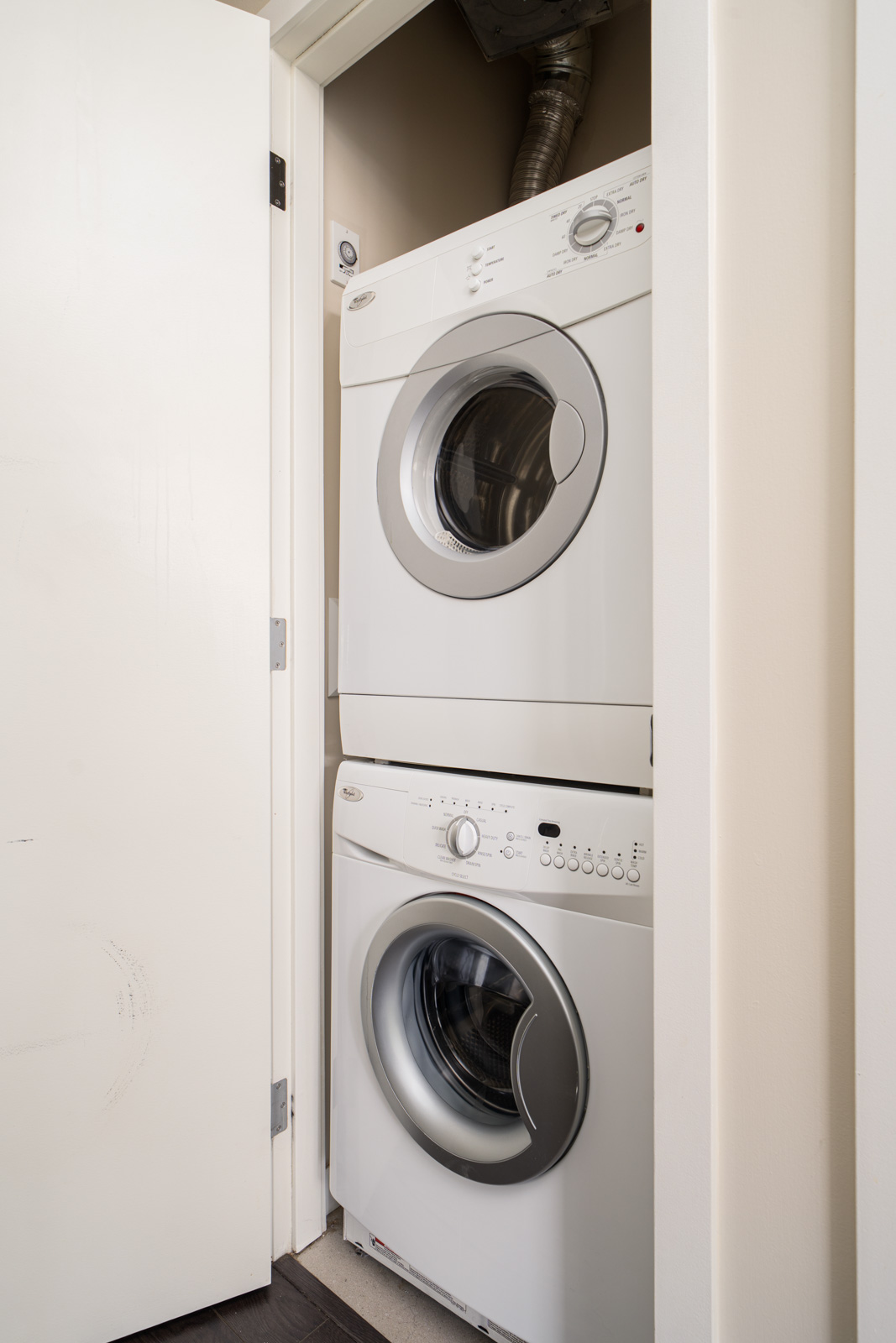 Stacked front-loading washer and dryer units are installed in a small closet with the door partially open.