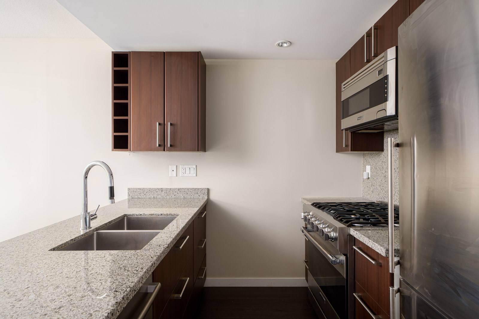 Modern kitchen with dark wood cabinets, granite countertops, stainless steel sink, gas stove, built-in microwave, and refrigerator.