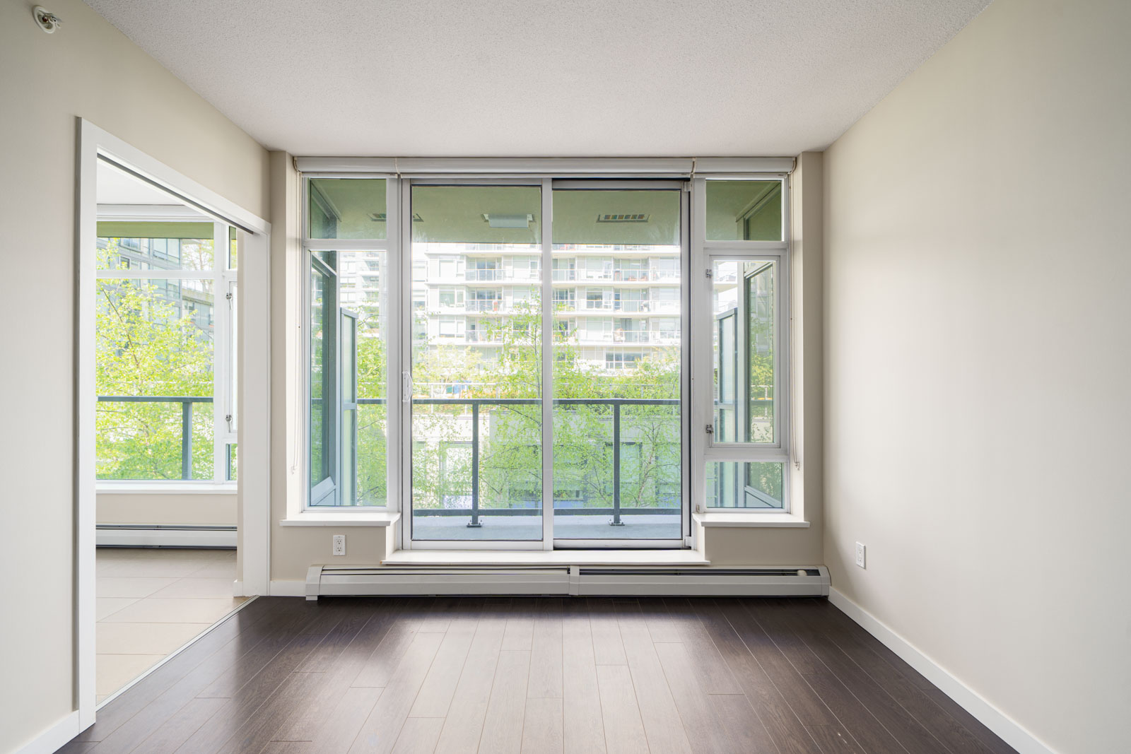 Unfurnished room with large floor-to-ceiling windows and glass door leading to a balcony, featuring light walls and dark hardwood flooring.