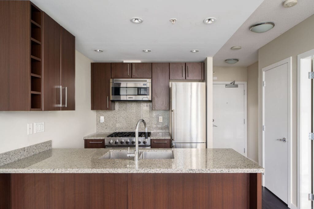 Modern kitchen with dark wood cabinets, stainless steel appliances, granite countertops, and a double sink on a large island.