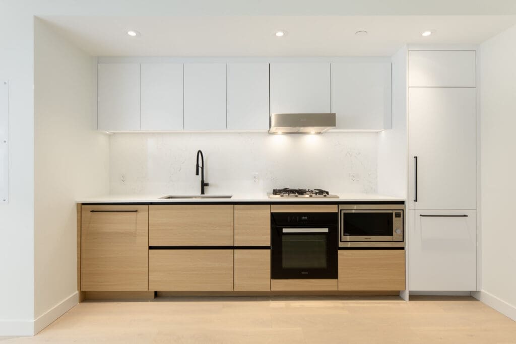 Modern kitchen with light wood lower cabinets, white upper cabinets, built-in appliances, a black faucet, and under-cabinet lighting.