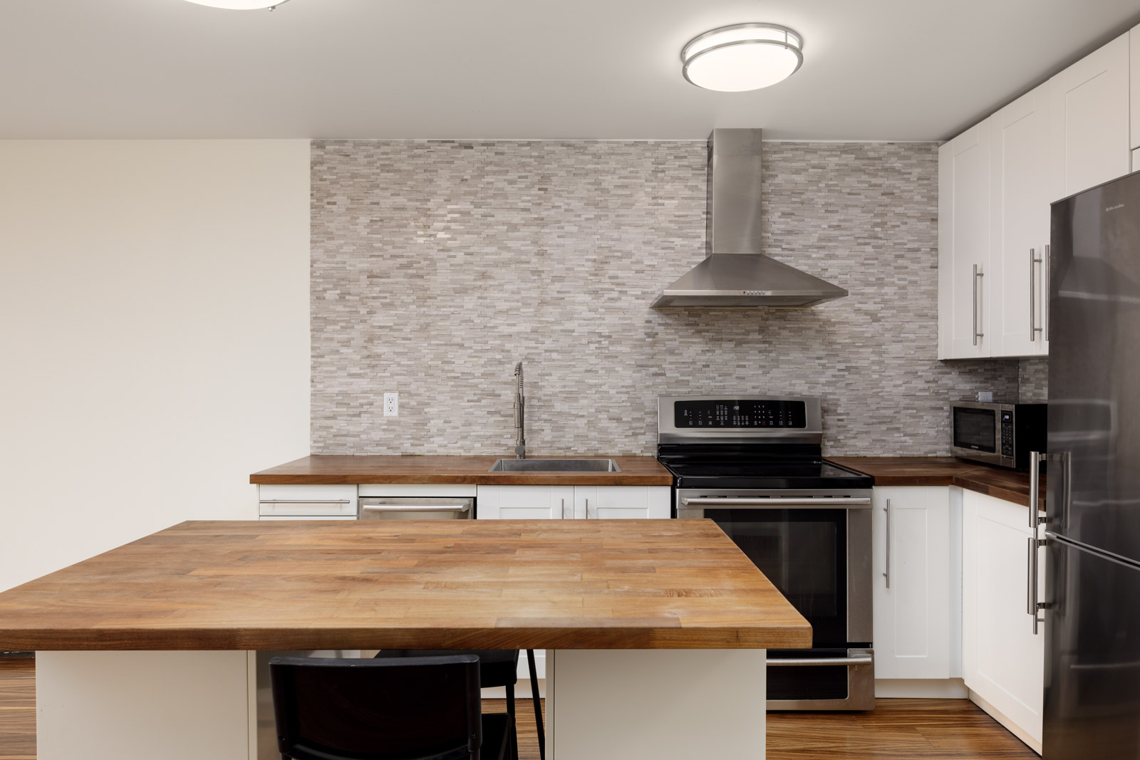 Modern kitchen with wood countertops, stainless steel appliances, a range hood, white cabinets, and a gray tiled backsplash.