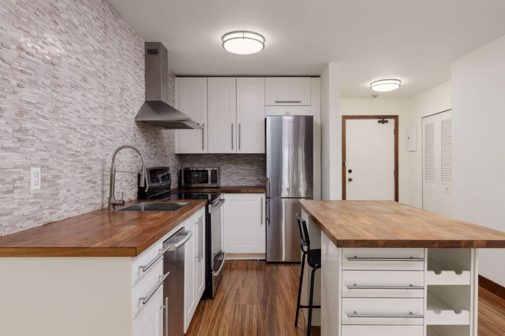 Modern kitchen with wooden countertops, stainless steel appliances, white cabinets, tile backsplash, and an island with open shelving and a bar stool.
