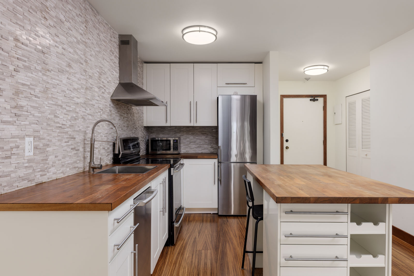 Modern kitchen with wooden countertops, stainless steel appliances, white cabinets, tile backsplash, and an island with open shelving and a bar stool.