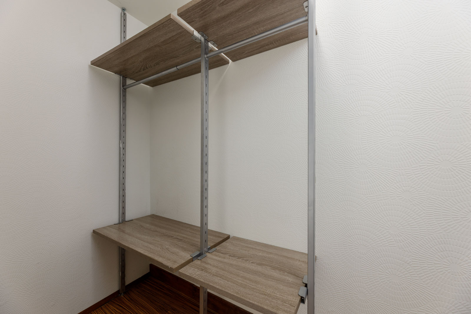 Empty closet with wood shelves and metal supports against white textured walls.