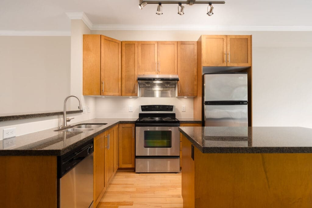 Modern kitchen with wood cabinets, stainless steel appliances, black countertops, an island, and a built-in sink and dishwasher.