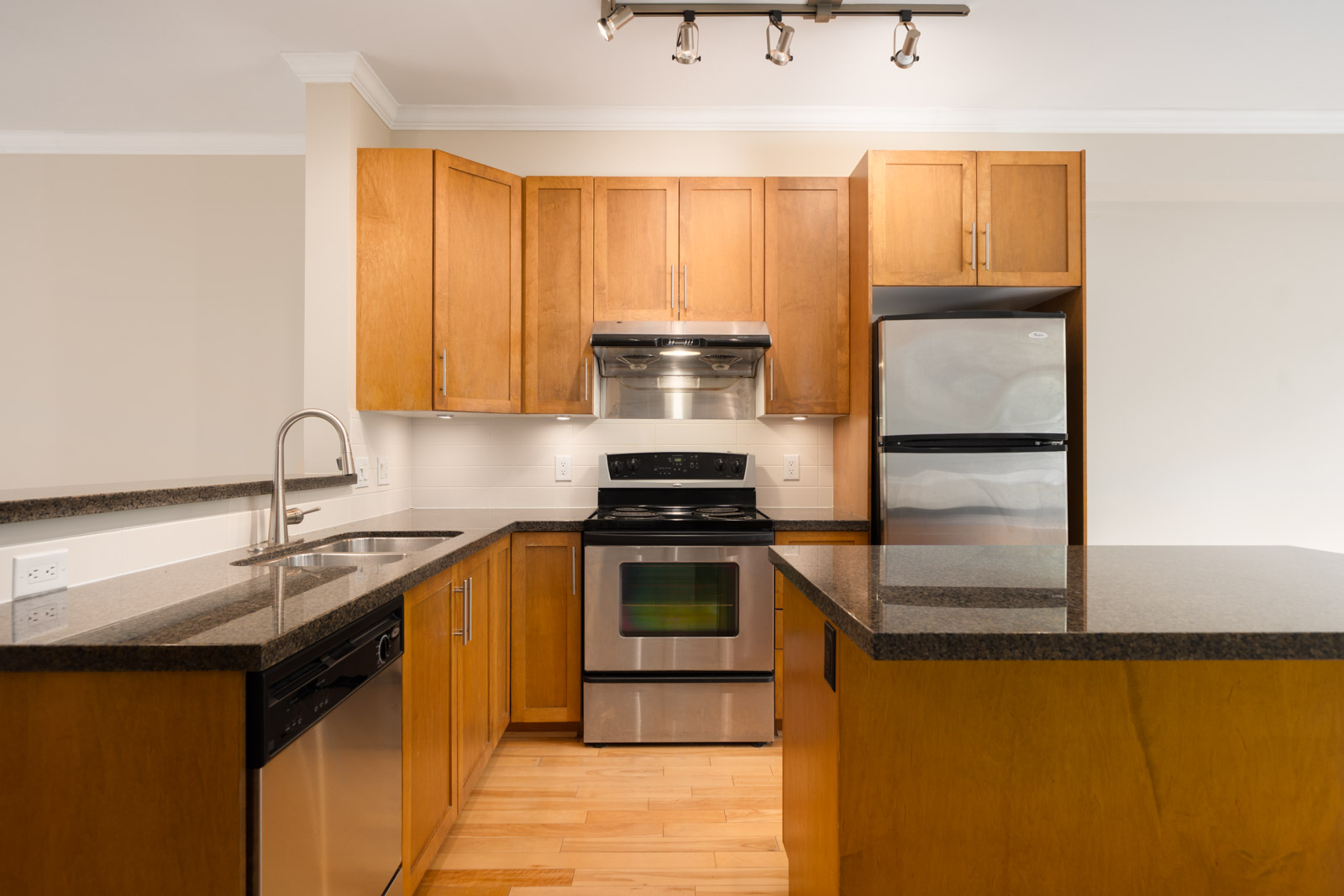 Modern kitchen with wood cabinets, stainless steel appliances, black countertops, an island, and a built-in sink and dishwasher.