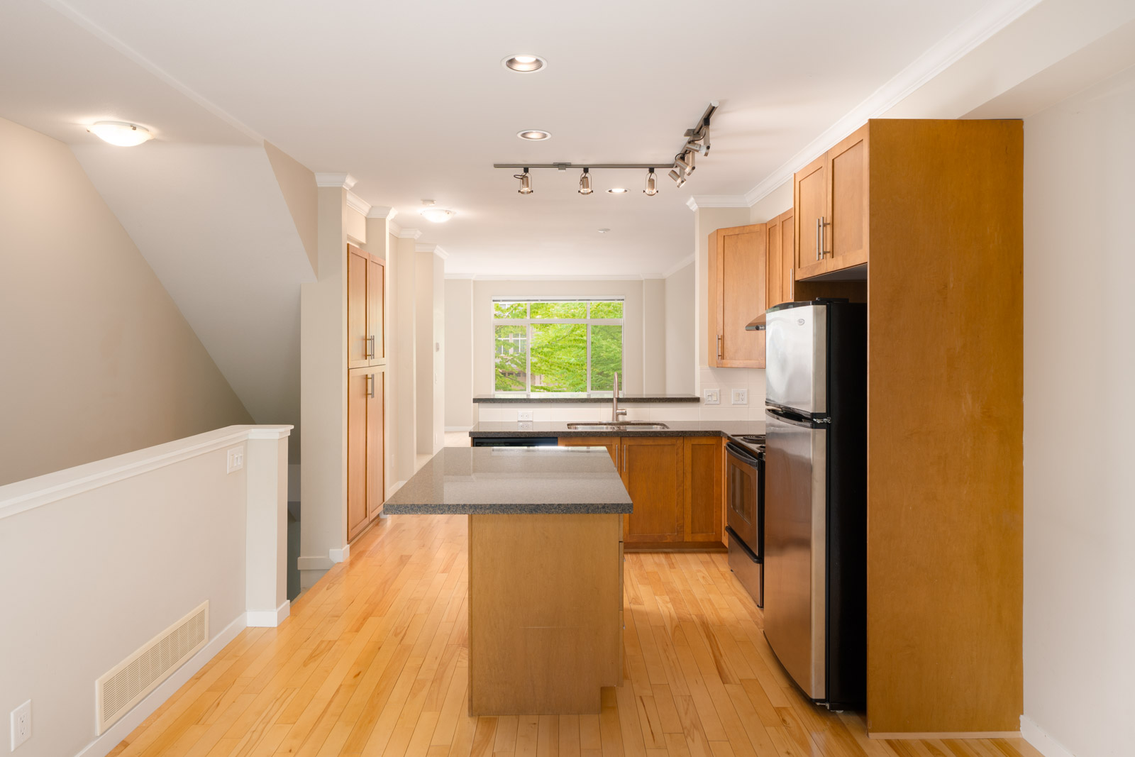 Modern kitchen with light wood floors, wood cabinets, stainless steel appliances, a center island, and a window above the sink letting in natural light.