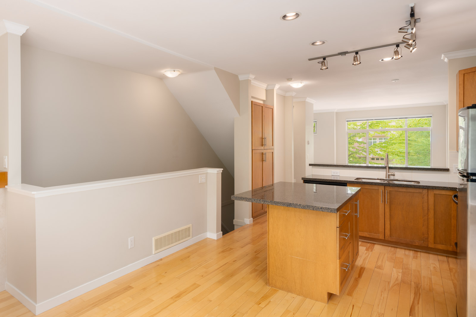 Modern kitchen with light wood floors, an island with a dark countertop, stainless steel appliances, and large windows letting in natural light.