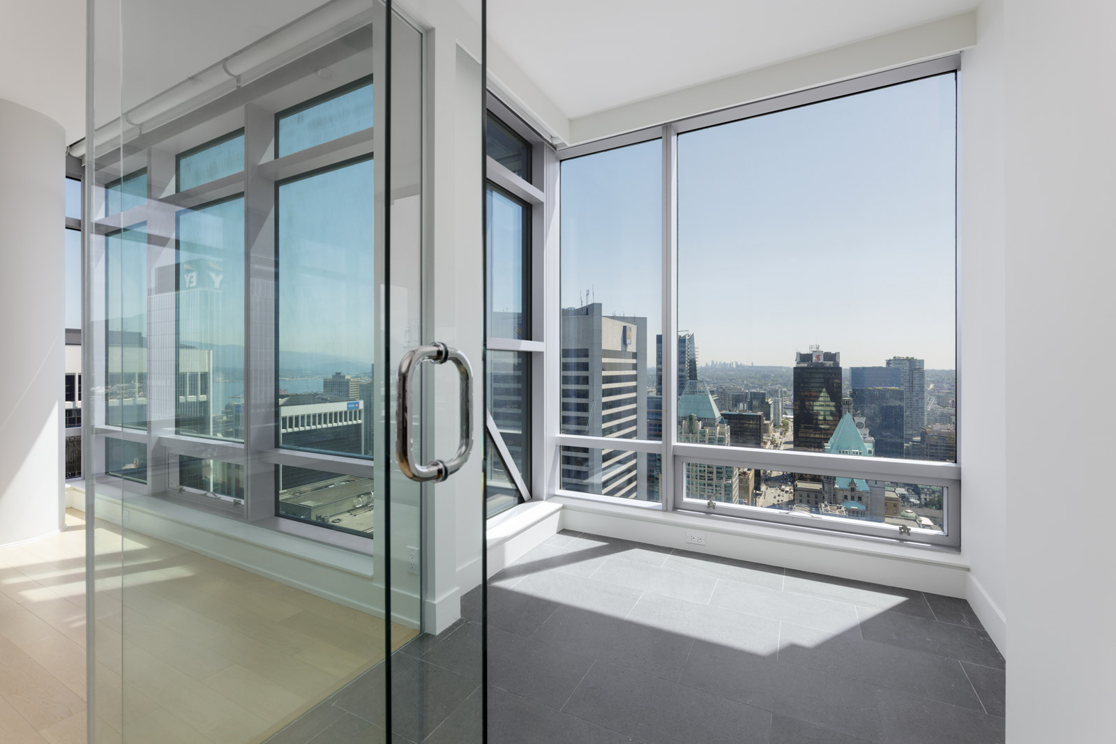 Corner office space with glass walls and large windows, offering a view of a cityscape with tall buildings under a clear sky.