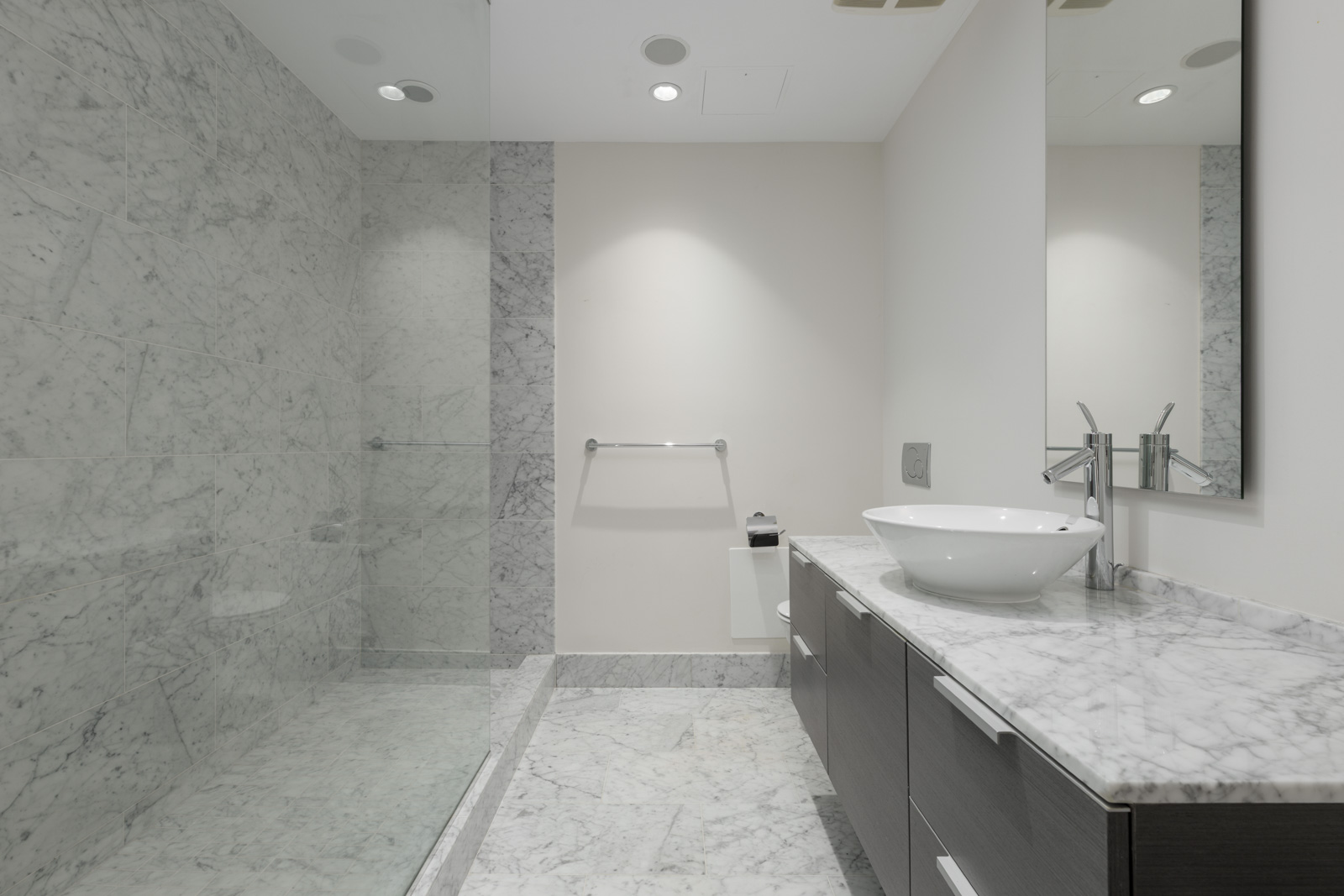 Modern bathroom with a marble countertop and sink, large mirror, walk-in glass shower, and marble walls and floor.