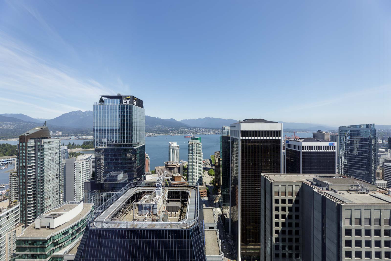 Aerial view of downtown city skyscrapers with mountains, harbor, and blue sky in the background.