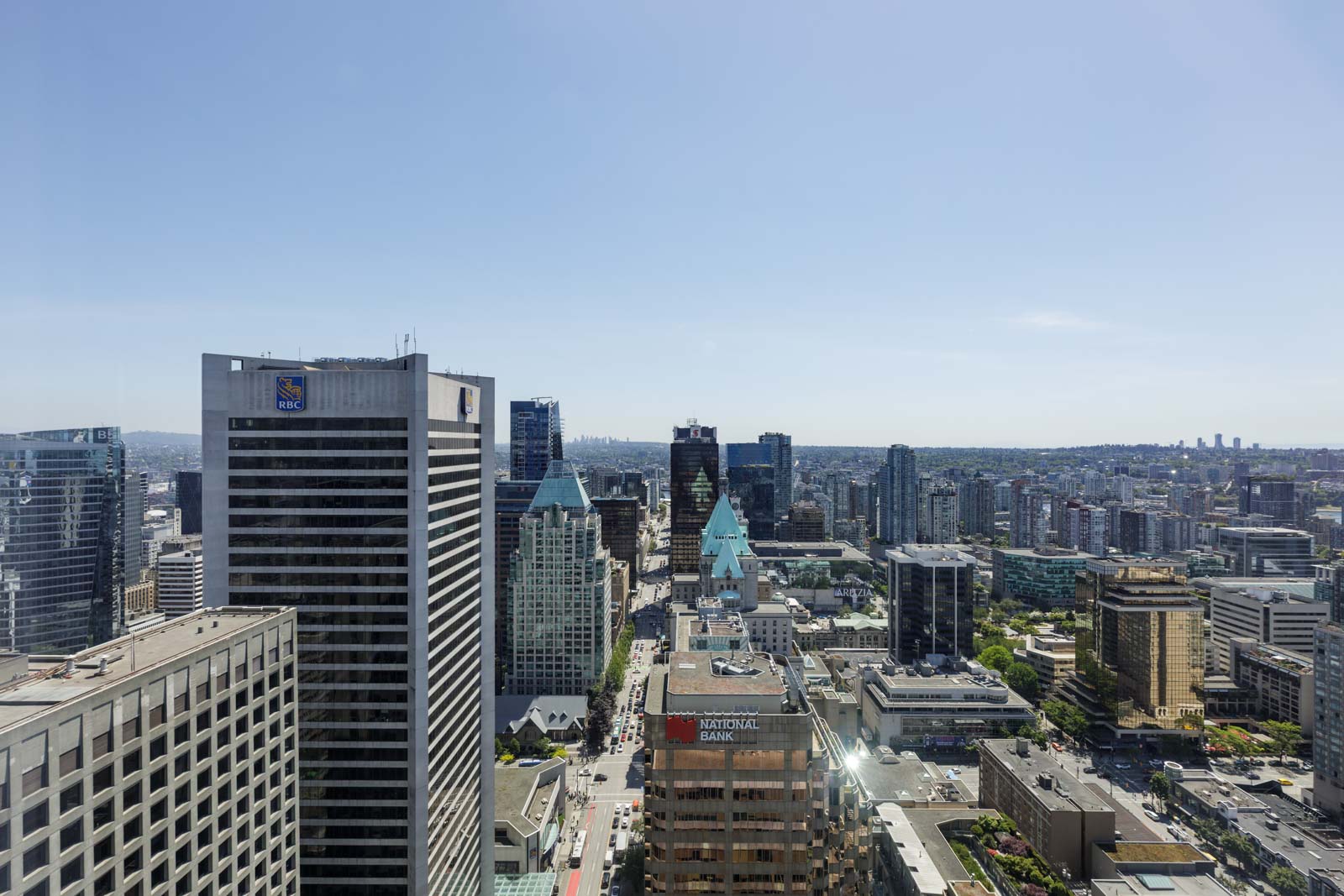 Aerial view of a cityscape with tall office buildings, modern skyscrapers, and busy streets under a clear blue sky.