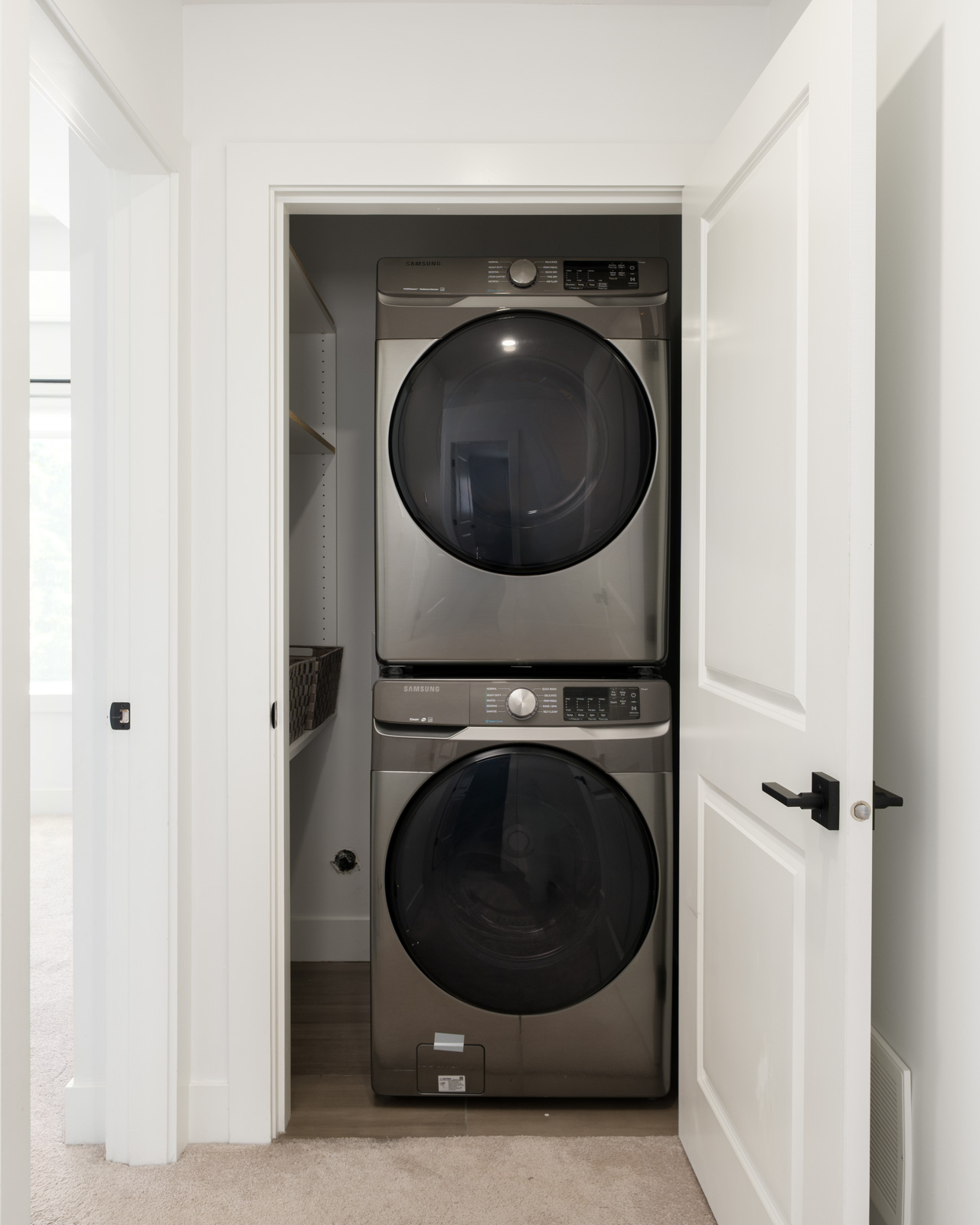 A stacked washer and dryer set is installed in a small closet with white doors, next to built-in shelving on one side.
