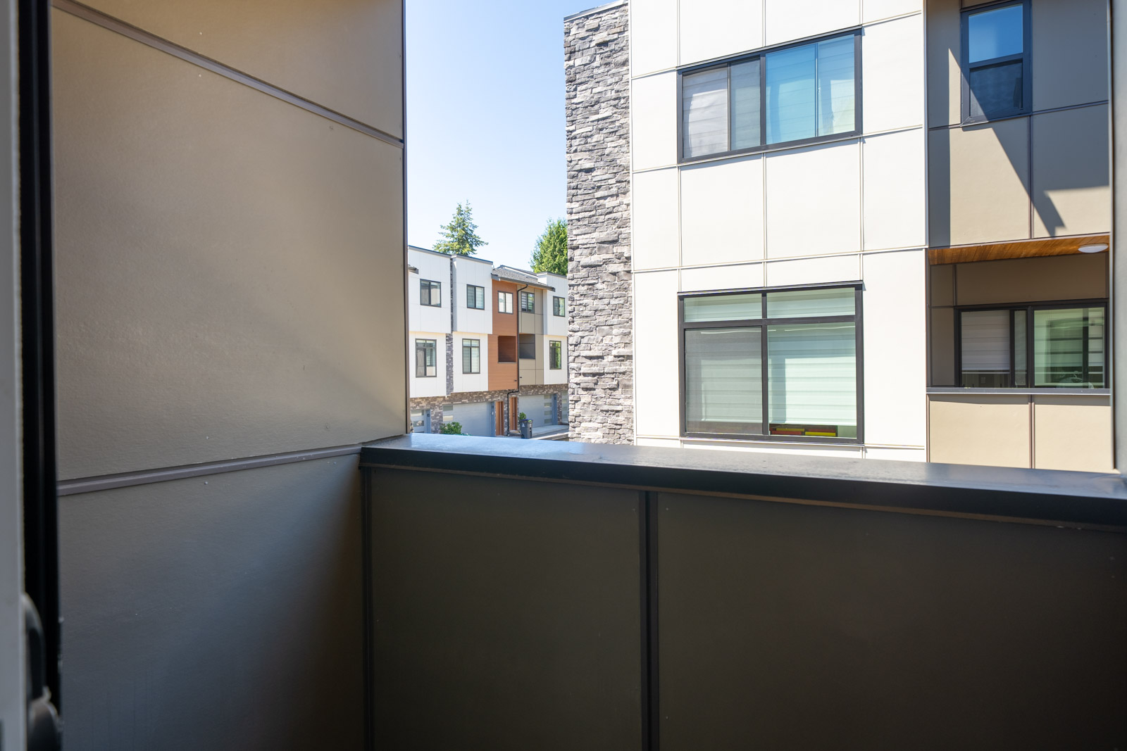 View from a balcony showing nearby modern apartment buildings with large windows and a courtyard area below on a bright day.