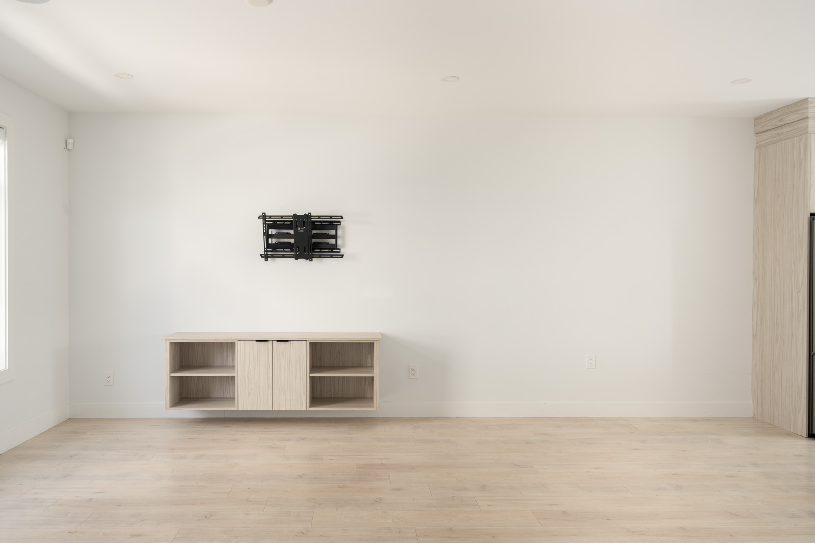Minimalist living room with light wood floors, a floating media console, and a TV wall mount on a plain white wall.