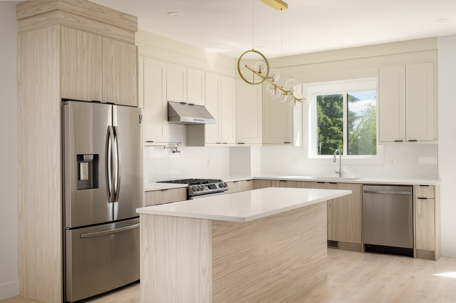 Modern kitchen with light wood cabinets, stainless steel appliances, a center island, white countertops, and a window above the sink.