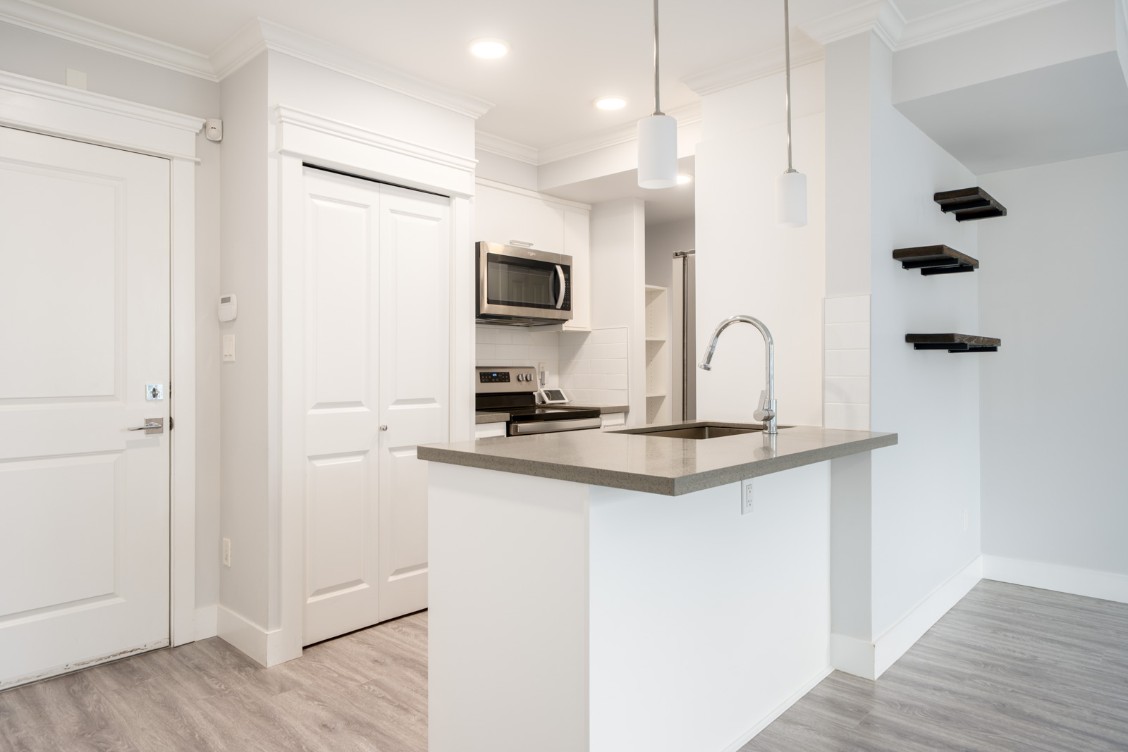 Modern kitchen with white cabinets, stainless steel appliances, a gray countertop island with sink, pendant lights, and floating black shelves on the wall.