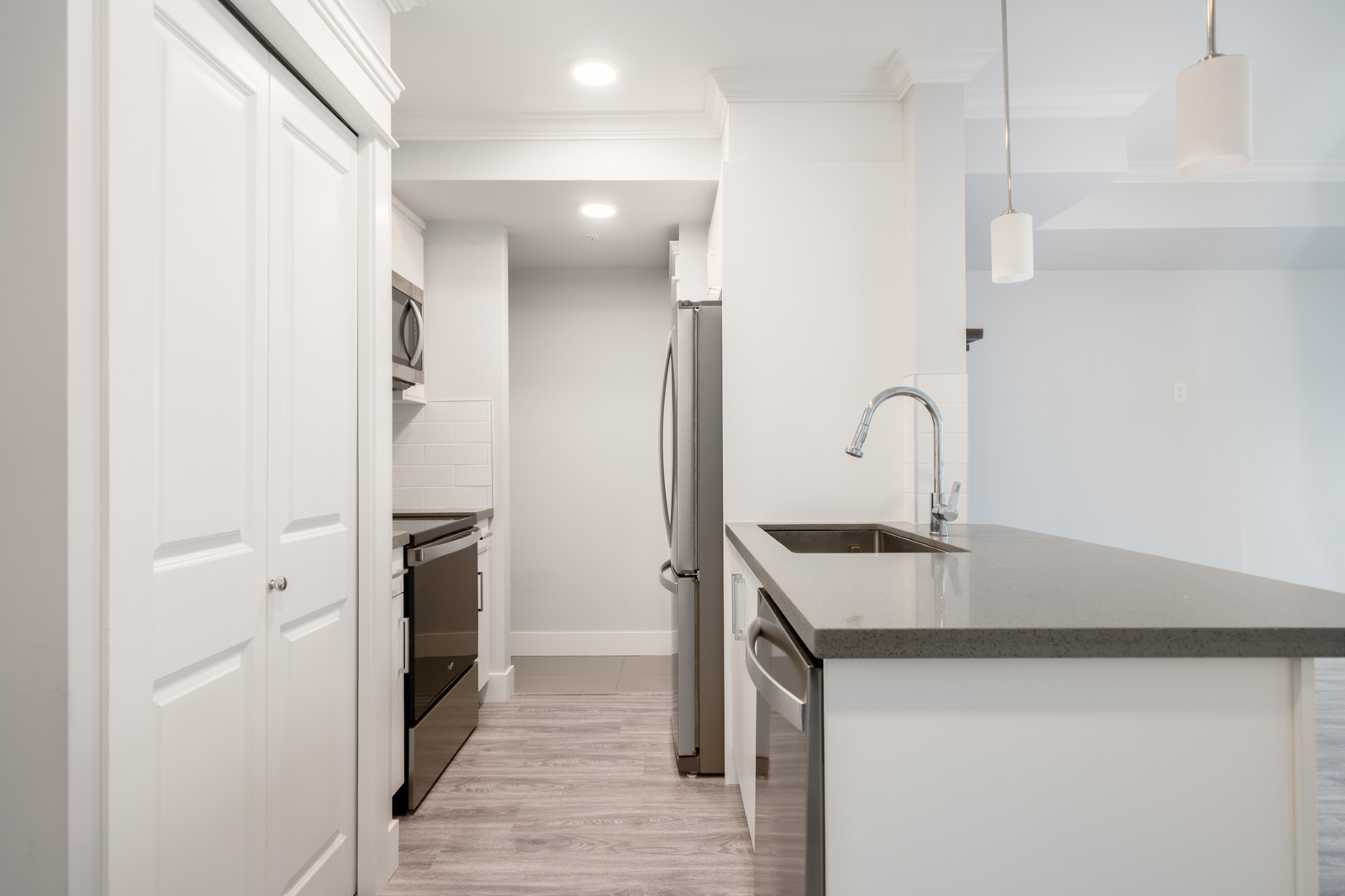 Modern kitchen with white cabinets, stainless steel appliances, undermount sink, and pendant lighting over a gray countertop island.
