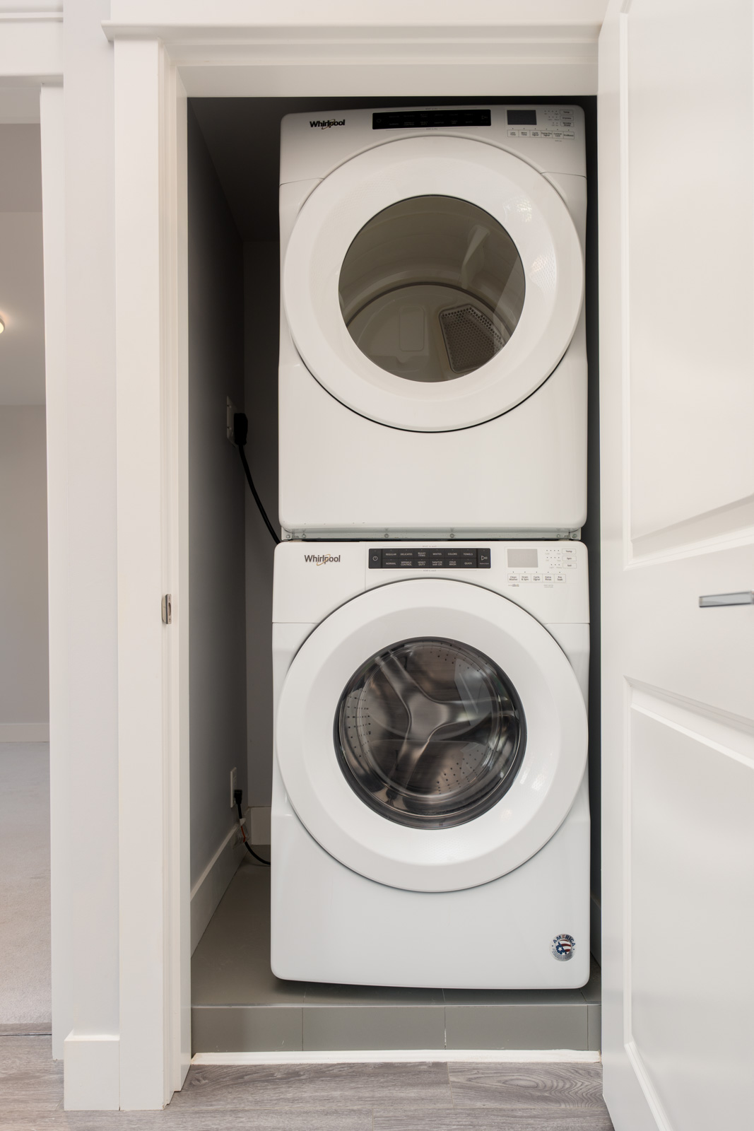 A stacked washer and dryer set in a small laundry closet with white doors and gray walls.